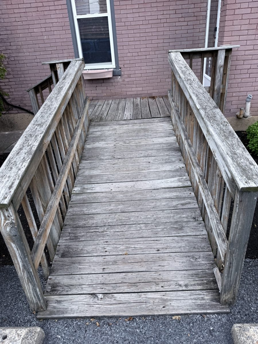 Weathered wood wheelchair ramp with gray, worn decking and railings before repair